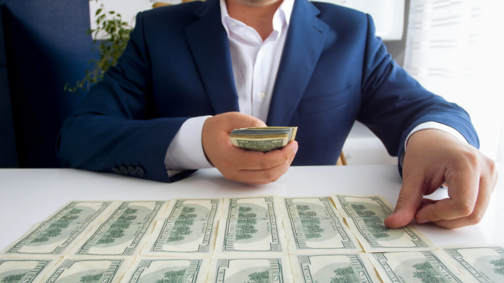 Closeup image of successful businessman laying money in front of him on office desk