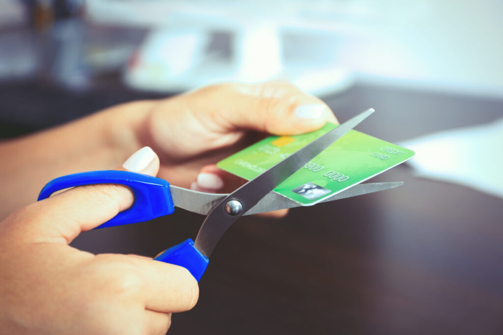 Woman's hands cutting bank card with scissors on wooden table background