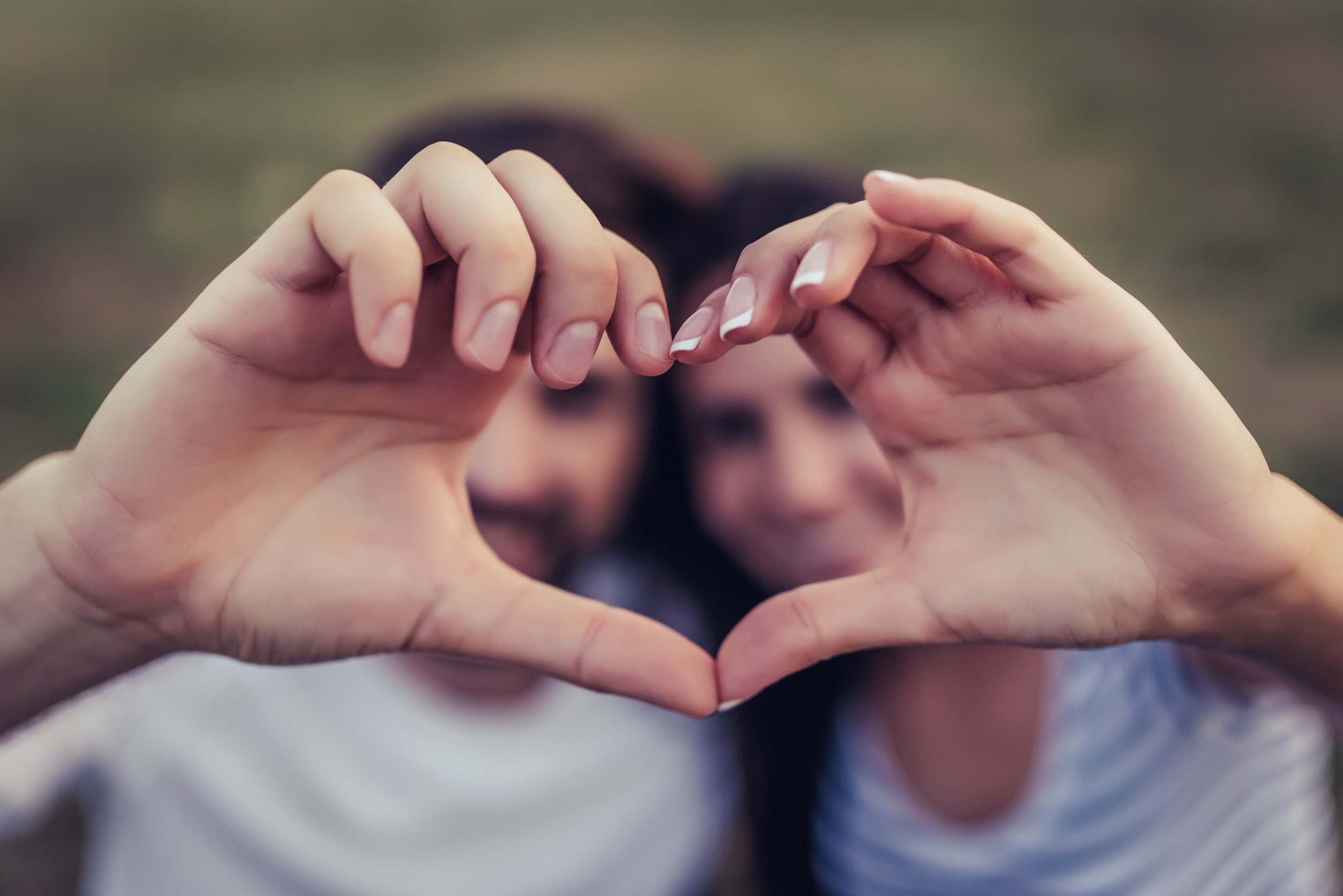 Beautiful romantic couple enjoying the company of each other outdoors. Making the heart sign from hands.