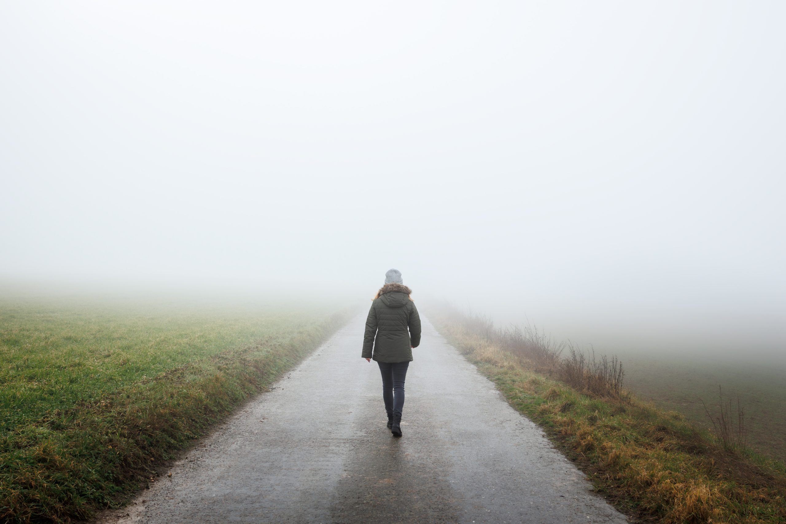 Lonely woman walks on empty road in fog. Journey to unknown place. Solitude female person walking outdoors