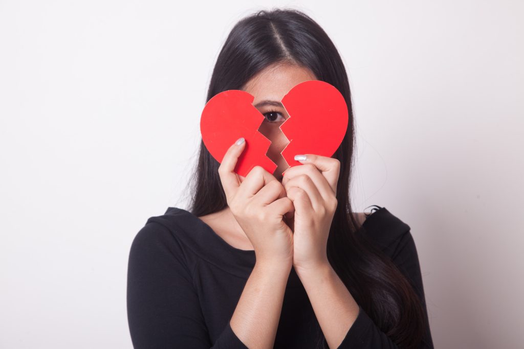 Beautiful young Asian woman with broken heart on white background