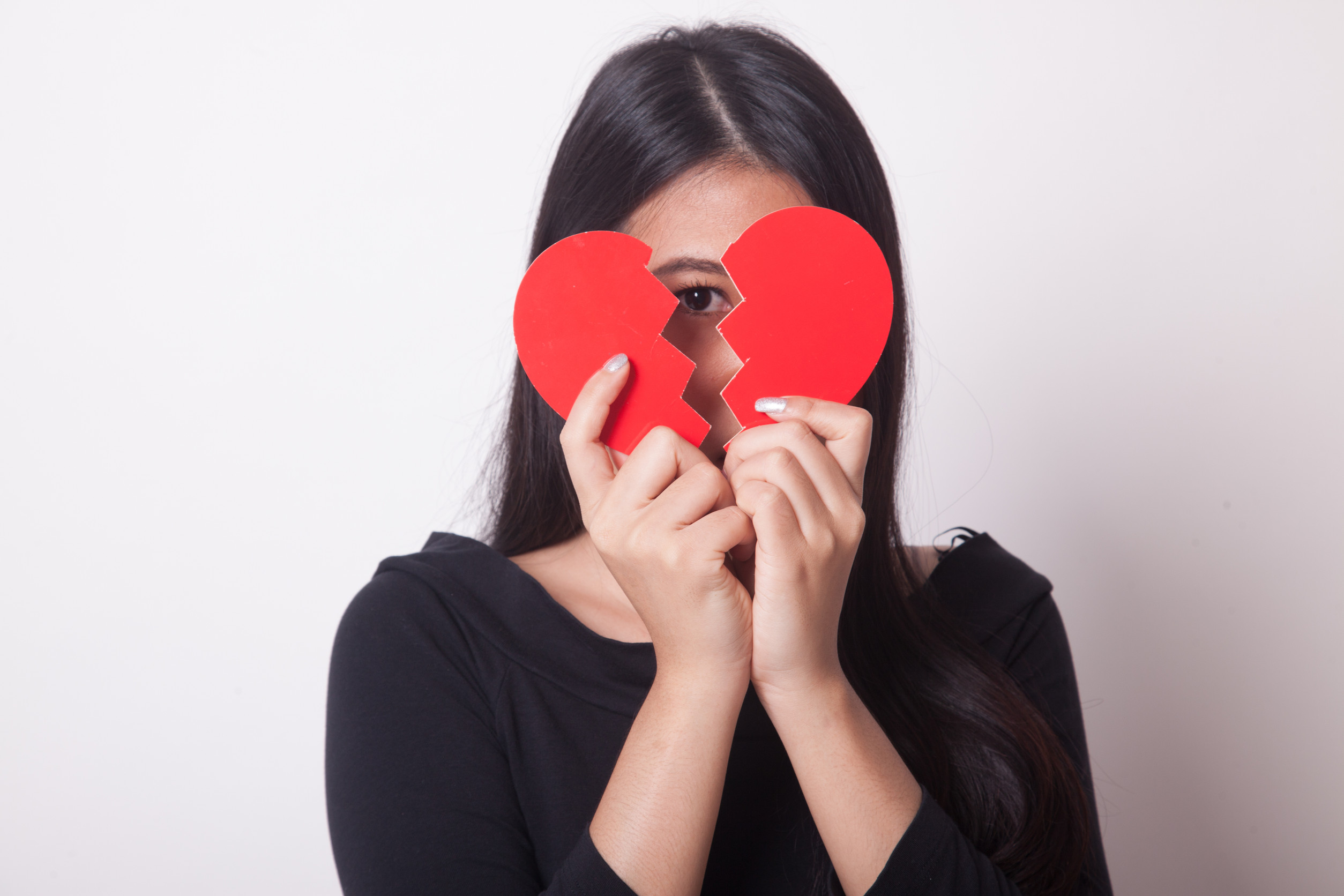 Beautiful young Asian woman with broken heart on white background