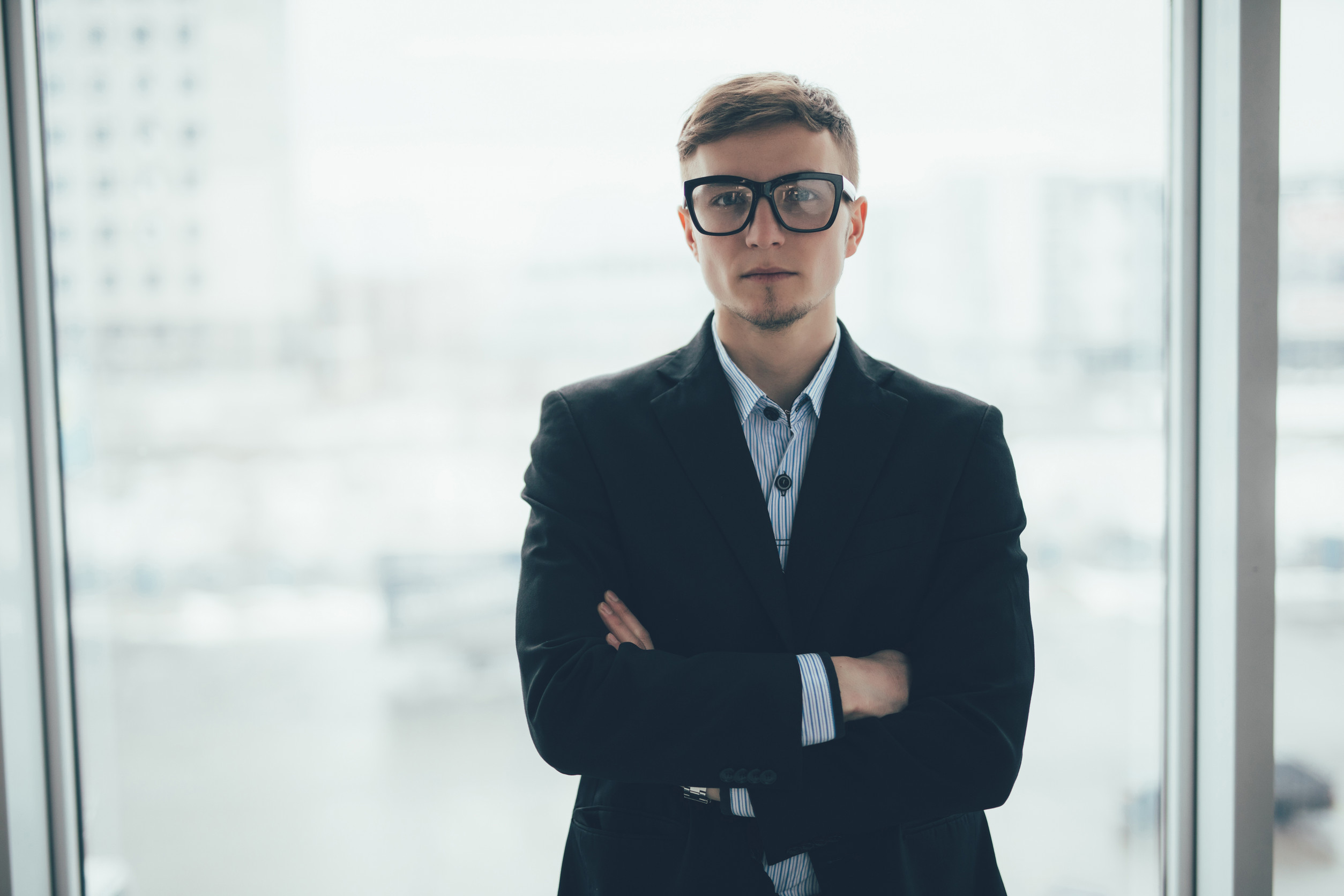 Confident businessman standing with arms folded at office