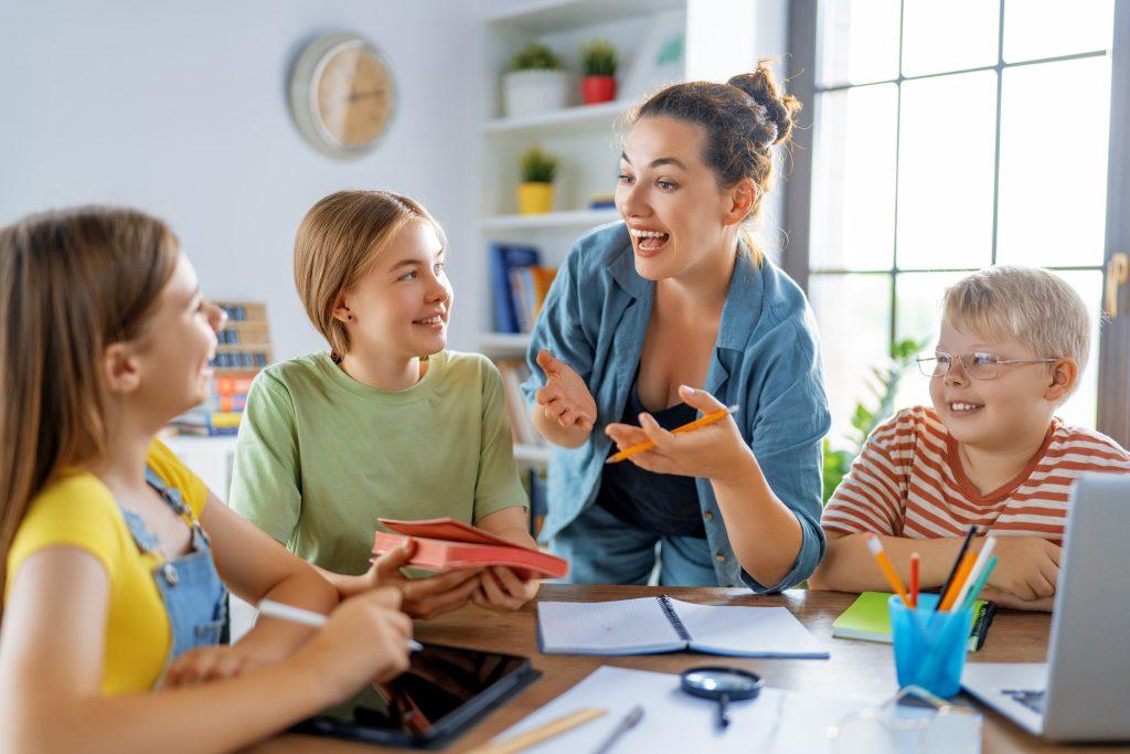 Happy kids and teacher at school. Woman and children are talking in the class.