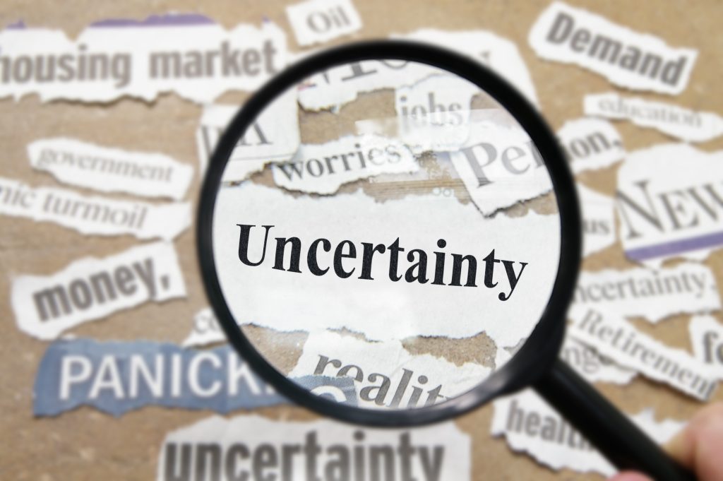 News headlines and magnifying glass with Uncertainty text