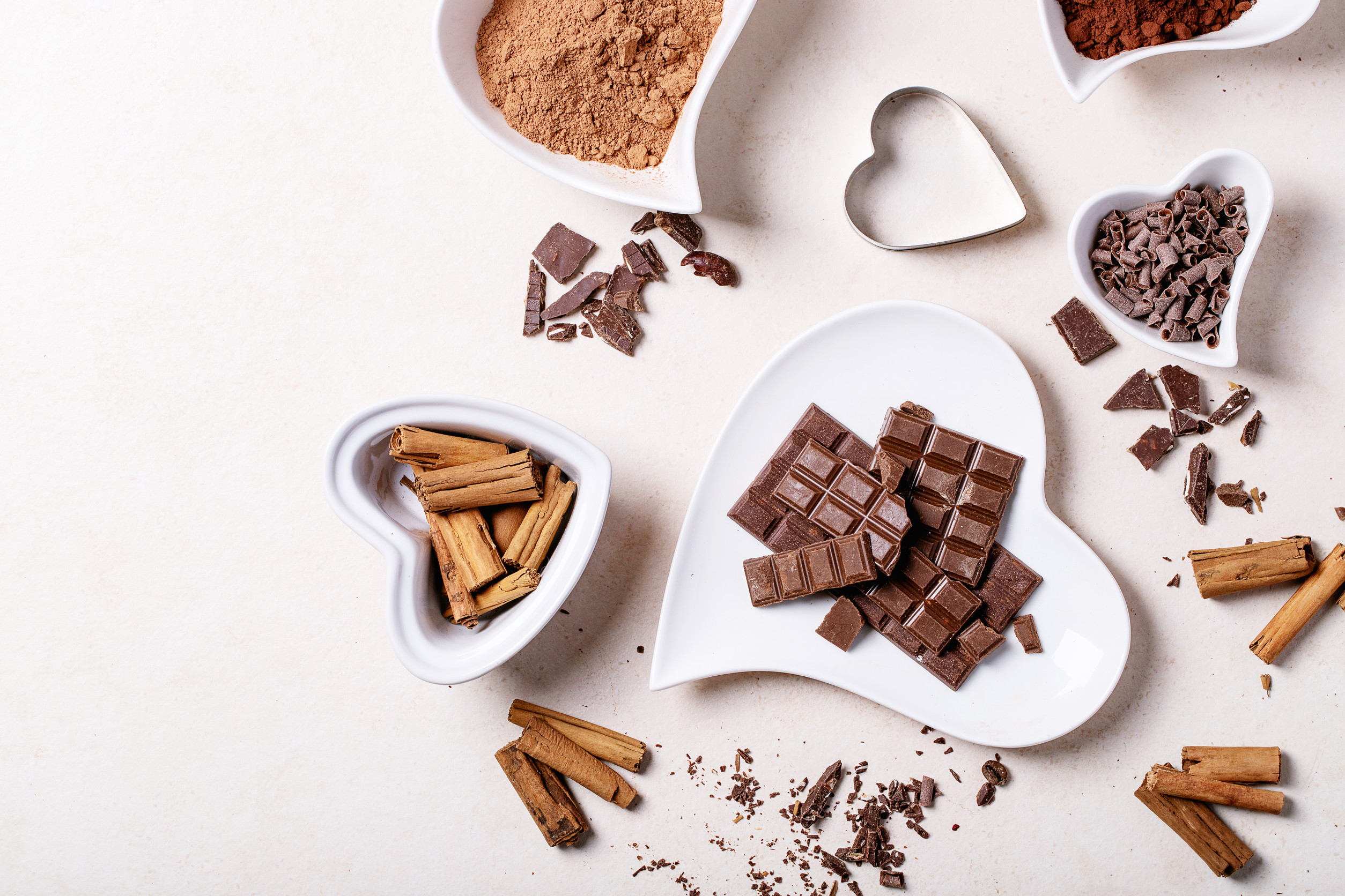 Saint valentine's day ceramic plates in shape of a heart with chocolate, cinnamon and cacao over white texture background. Top view, flat lay. Copy space