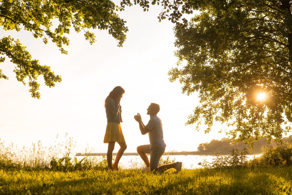 Loving man making a wedding offer to his beautiful girlfriend. Be my wife concept. Field and sea background.