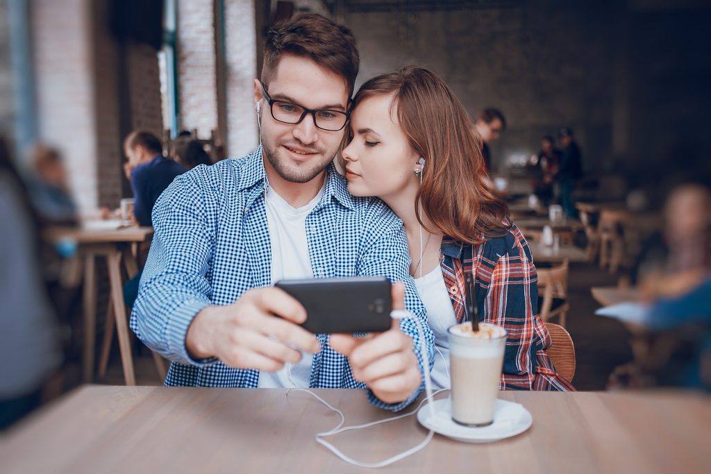 The boy and girl resting in cafe, photographed on the phone and listening to music on headphones