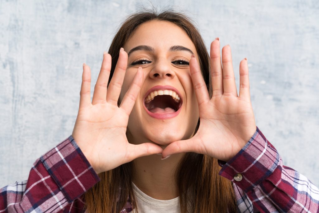 Young woman over textured wall shouting with mouth wide open
