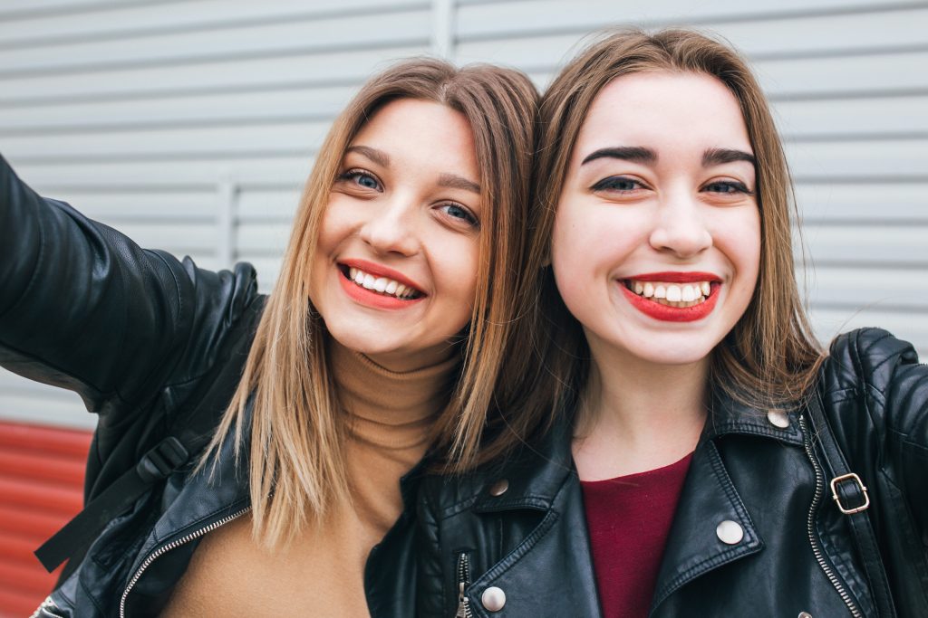 Two young girls taking selfie using smartphone in city