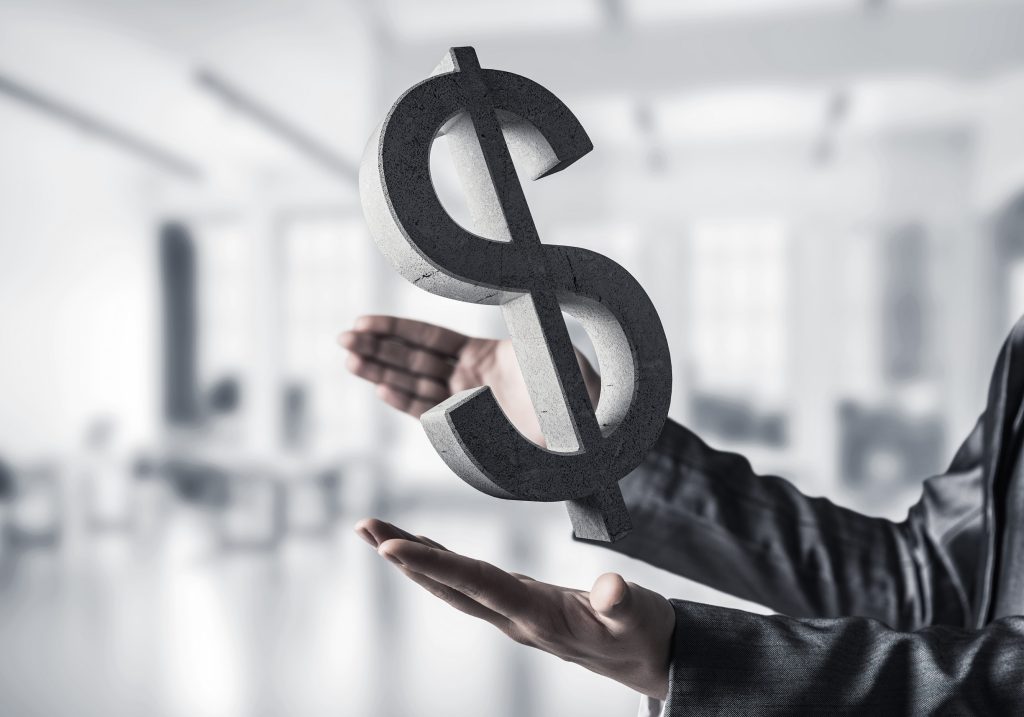 Closeup of business woman in black suit keeping stone dollar sign in hands with office view on background. Mixed media.