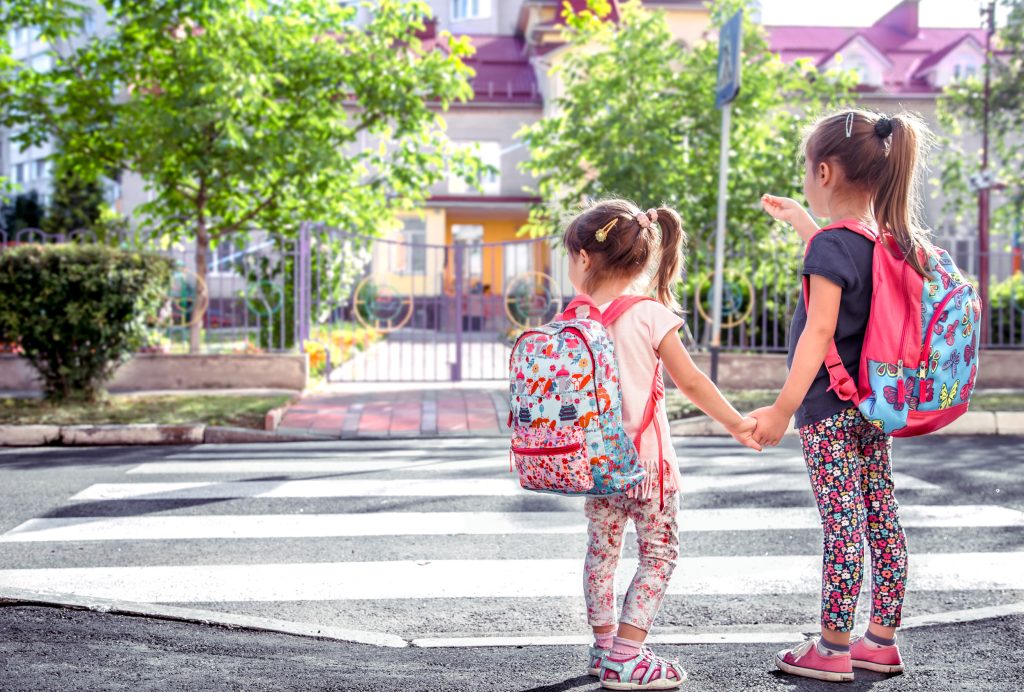 Children go to school, happy students with school backpacks and holding hands together, cross the road, the concept of education with girls, space for text