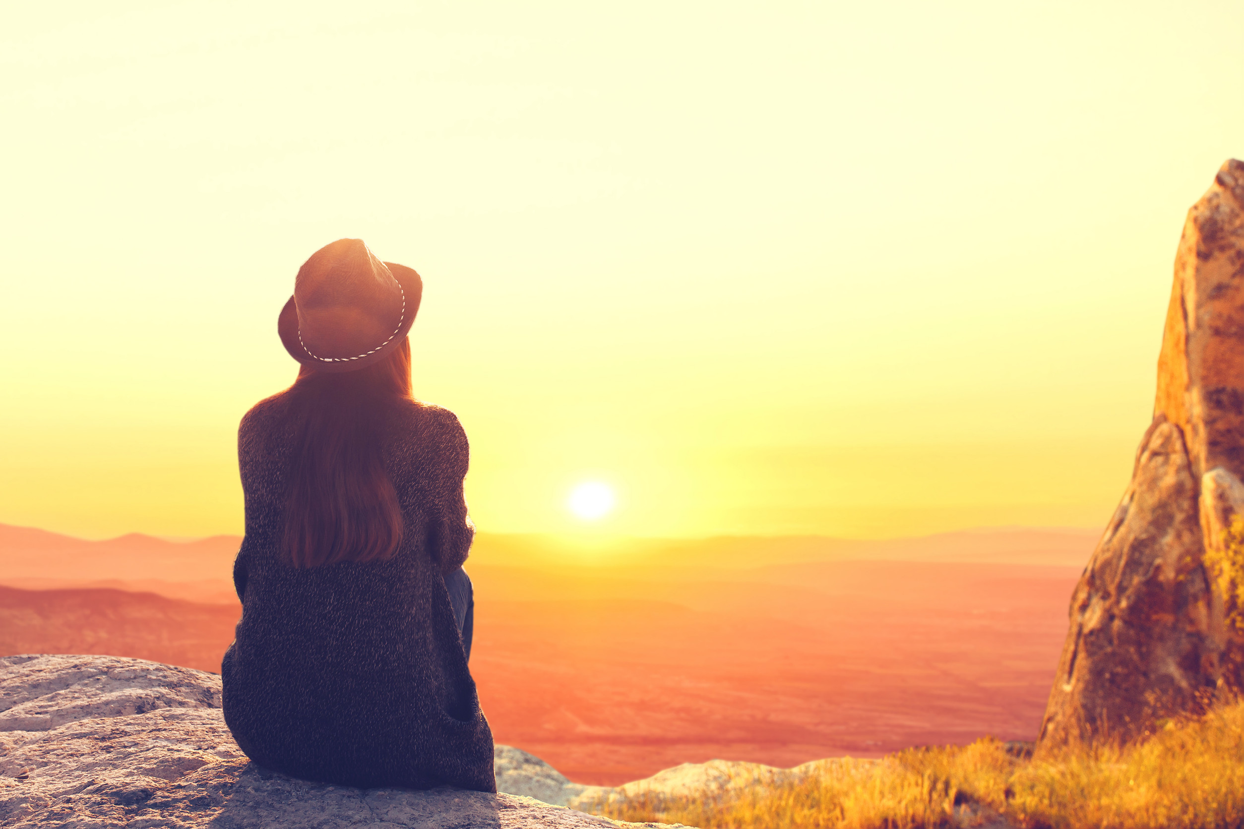A woman sits on top of a mountain and admires the beautiful natural landscape. Digital detox and soul search. Unplugged