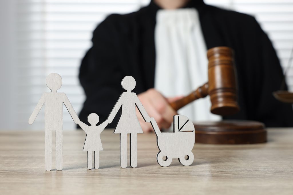 Family law. Judge with gavel sitting at wooden table, focus on figure of parents and children