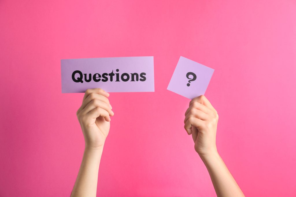 Woman holding sheets of paper with word QUESTIONS and query mark on pink background, closeup