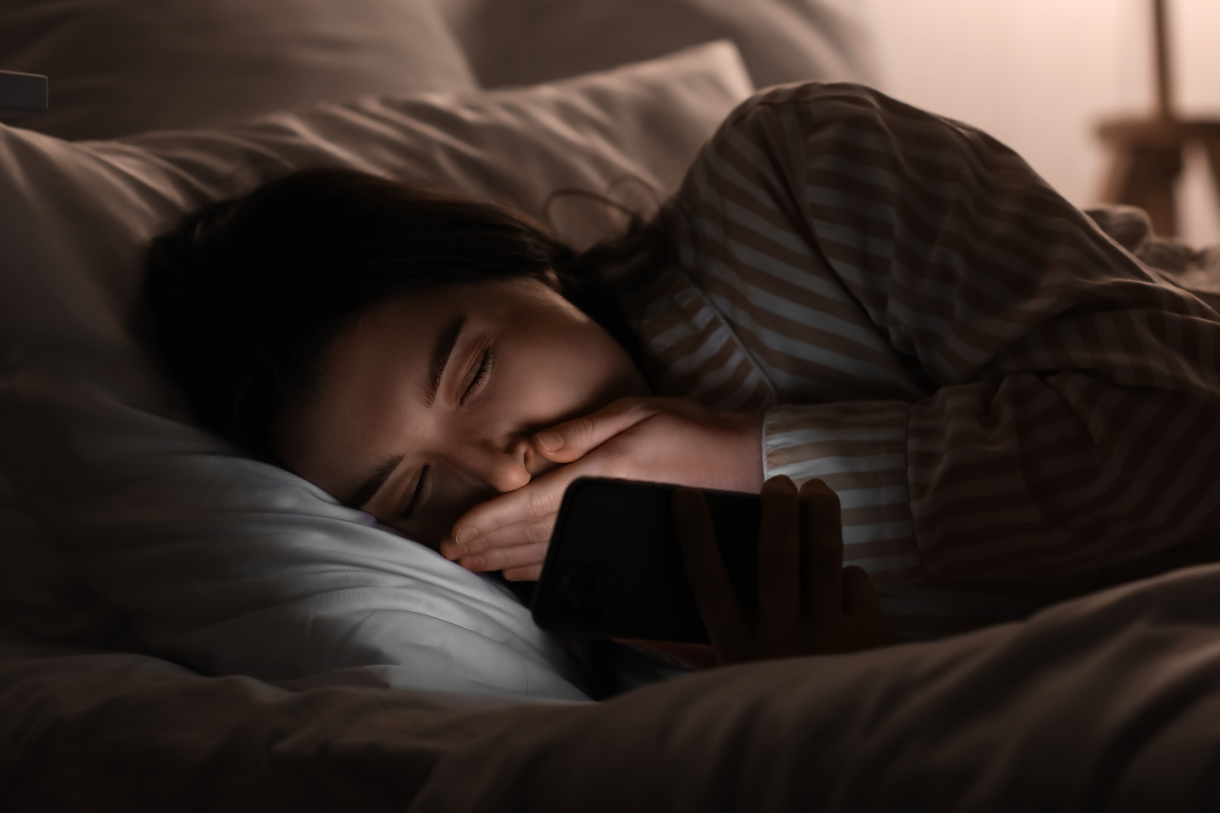 Young woman using mobile phone in bed at night, closeup